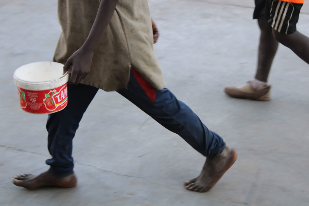 Pieds nus, sébile en main, un garçon mendie pour nourrir son maître au Sénégal.